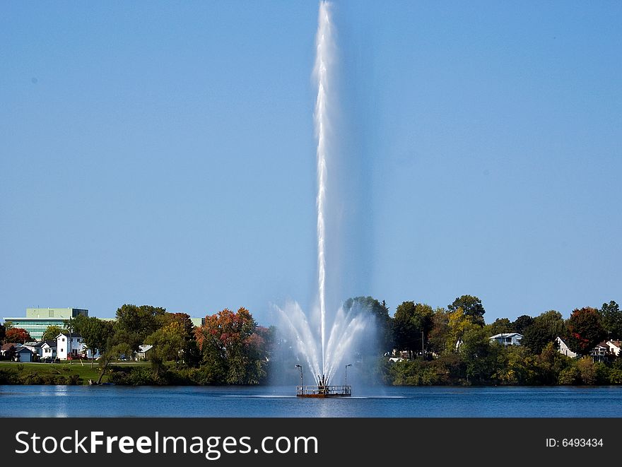 A tall fountain showers the middle of a lake. A tall fountain showers the middle of a lake