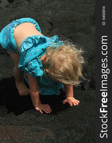 Little girl playing in black sand with her hawaii dress on. Little girl playing in black sand with her hawaii dress on