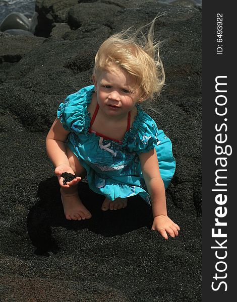 Blonde little girl with black sand in her right hand as the wind blows her hair