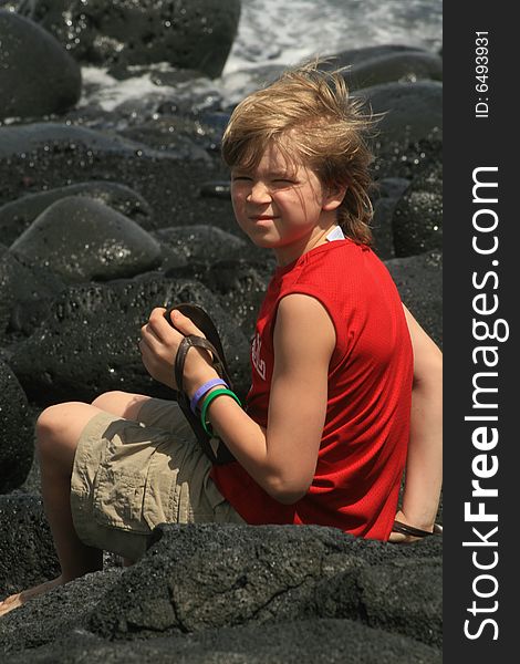 Young boy sitting on lava while playing in black sand. Young boy sitting on lava while playing in black sand