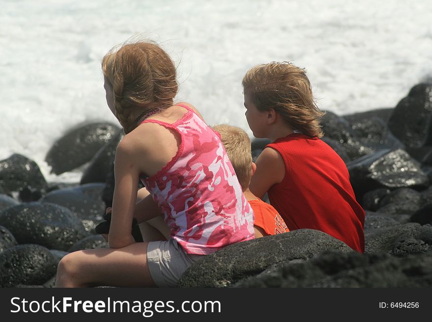 Brothers and sister sitting on lava rocks while watching the waves