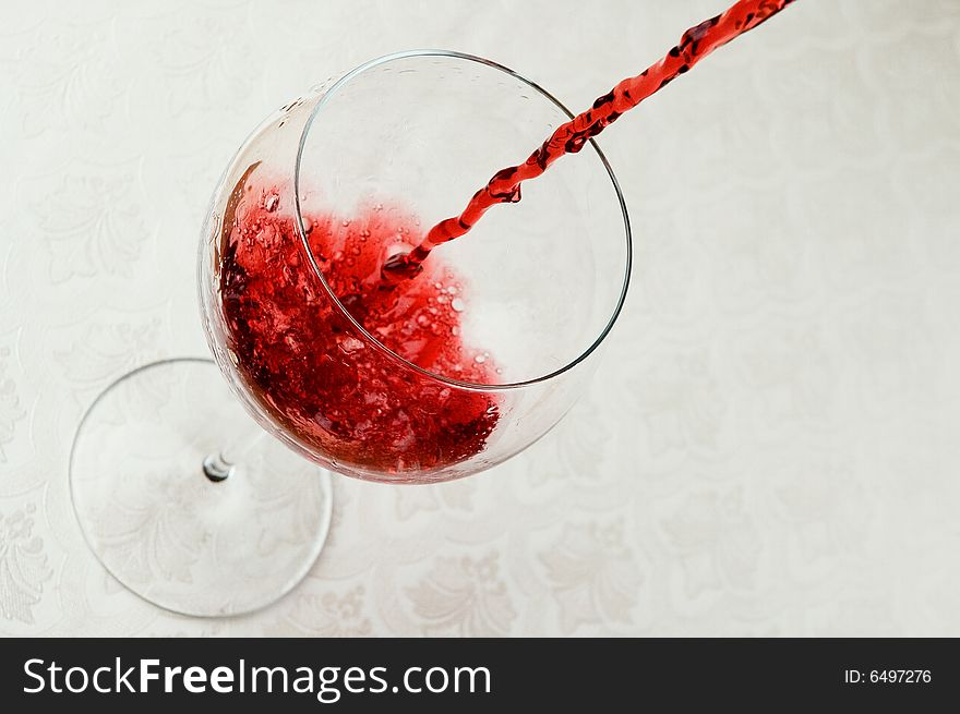 Red wine waterfall in glass on white table