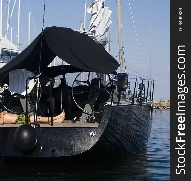 Black sailboat docked in the harbor and a man sleeping on the deck. Black sailboat docked in the harbor and a man sleeping on the deck