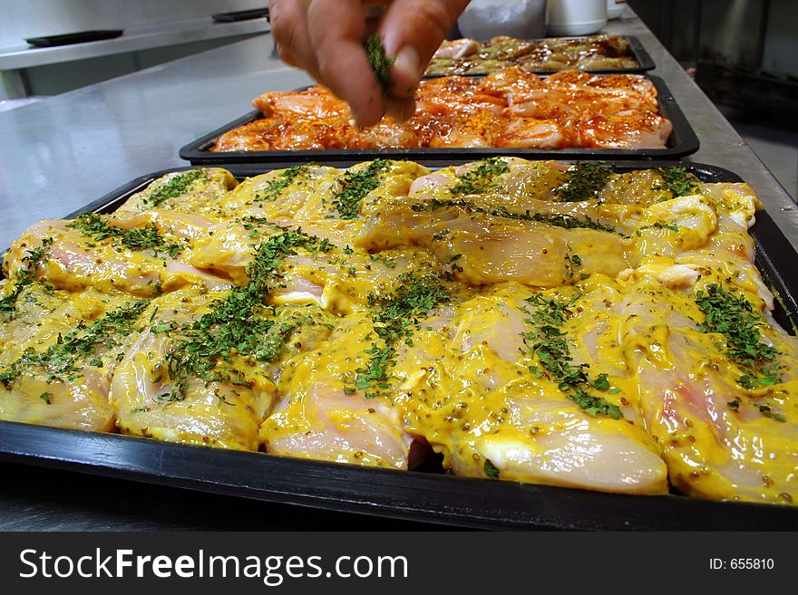 A tray of fresh chicken fillet steaks covered in a delicious mustard sauce being coated with fresh herbs. A tray of fresh chicken fillet steaks covered in a delicious mustard sauce being coated with fresh herbs