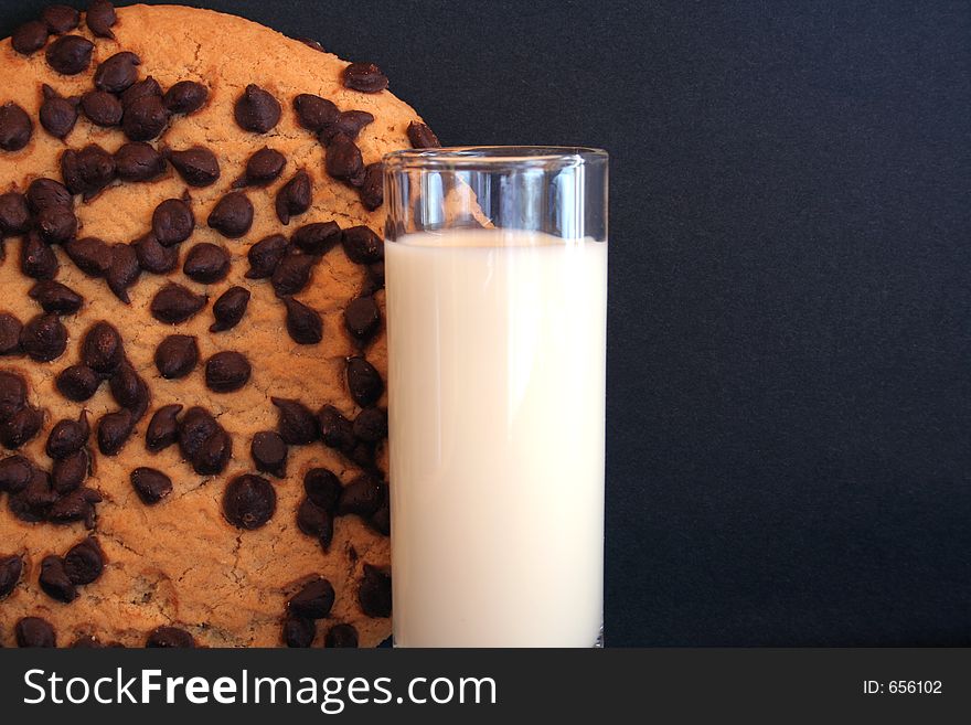 Image of a giant chocolate chip cookie next to a shot glass of milk - room for text. Image of a giant chocolate chip cookie next to a shot glass of milk - room for text