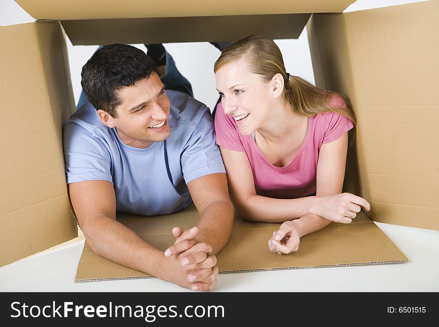 Young smiling couple lying in cardboard box and talking. Front view. Young smiling couple lying in cardboard box and talking. Front view.