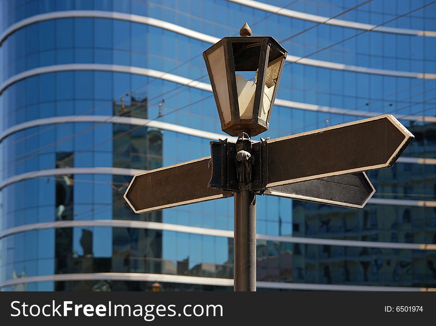 Blank signpost with ancient lamp against business building