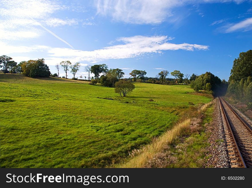 Green meadow with trees next to rail track and blue cloudy sky. Green meadow with trees next to rail track and blue cloudy sky