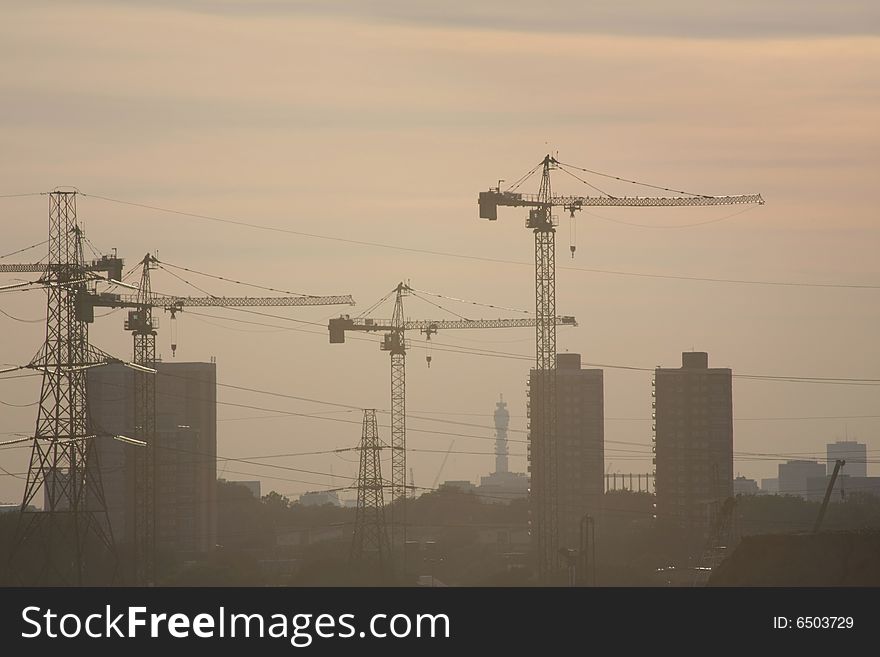 In the mist the silhouette of three cranes in a construction area, between some high buildings