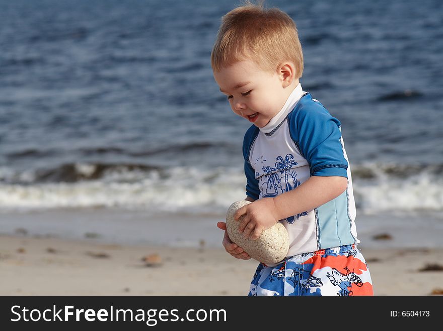 A toddler carrying a large rock on a sandy beach. A toddler carrying a large rock on a sandy beach.