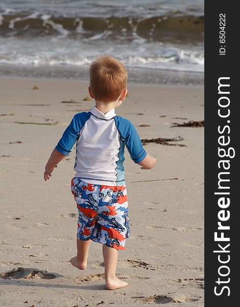 A toddler boy running towards the water on a sandy beach. A toddler boy running towards the water on a sandy beach.