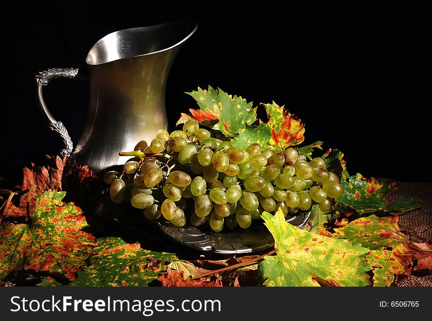 Grapes with metal jug and fall leaves on burlap background. Grapes with metal jug and fall leaves on burlap background