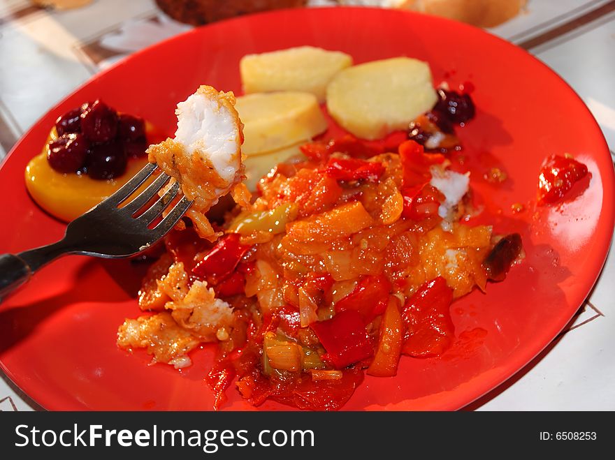 Fish on fork over fried vegetables plate. Fish on fork over fried vegetables plate