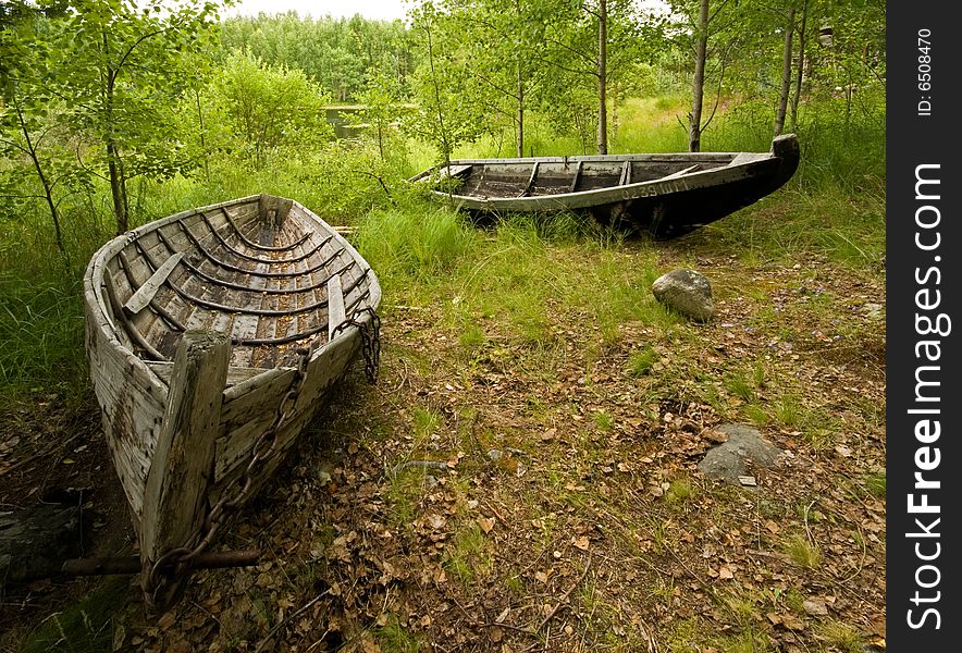 Two old wooden boats lie close to the bank of a lake. Two old wooden boats lie close to the bank of a lake