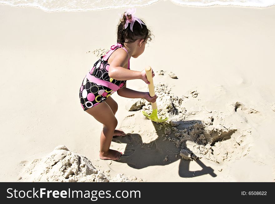 Little girl working hard shoveling sand at the beach dressed in her swimsuit.