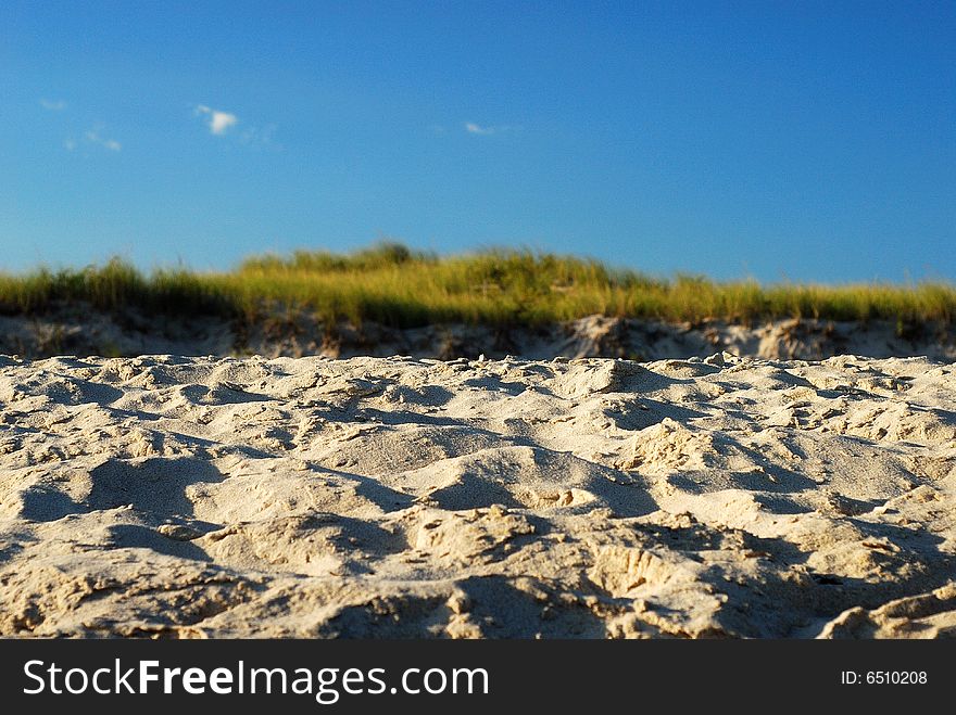 This is a shot of a sandy beach looking towards a grassy knoll and blue sky with small plumes of cloud.