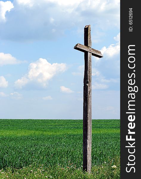 A wooden cross stands in an empty green field. A wooden cross stands in an empty green field