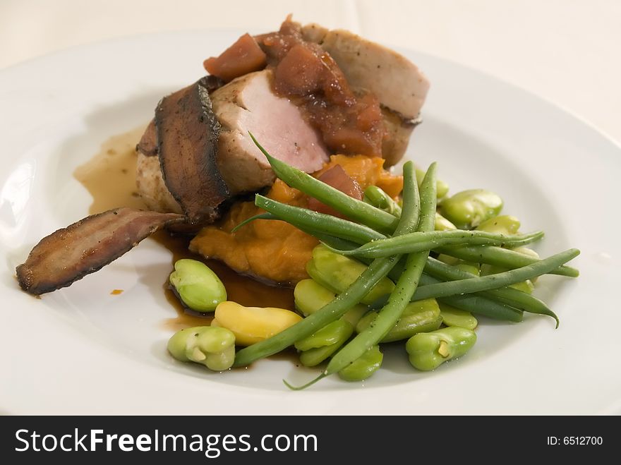 Pork loin wrapped with bacon over candied yams green and fava beans
