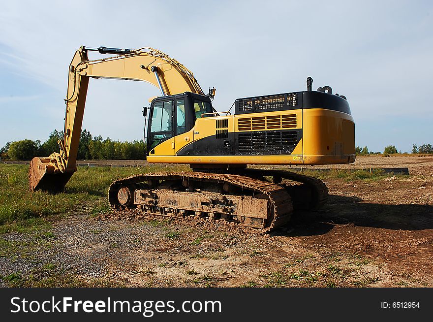 An yellow heavy excavator sitting on an field to begin construction of an industrial site. An yellow heavy excavator sitting on an field to begin construction of an industrial site.