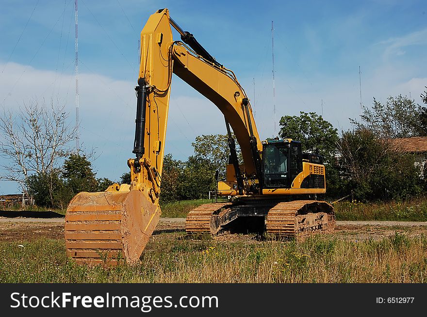 An yellow heavy excavator sitting on an field to begin construction of an industrial site. An yellow heavy excavator sitting on an field to begin construction of an industrial site.