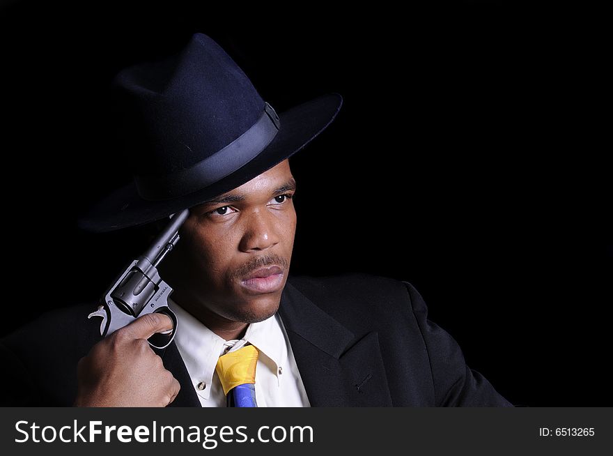 Young African American man in a hat and suit with gun to his head isolated on black