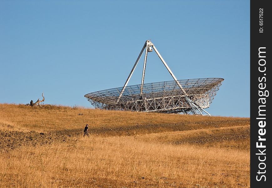 The Stanford satellite dish sits on top of a hill as a man hikes to the top. The Stanford satellite dish sits on top of a hill as a man hikes to the top.