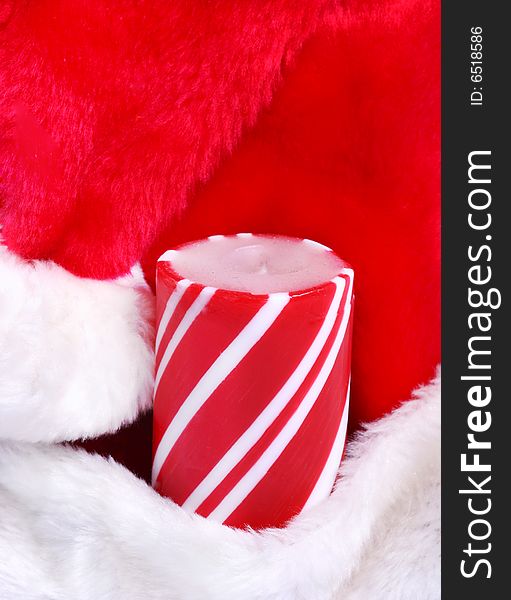 A striped candle nestled in a Santa's hat. A striped candle nestled in a Santa's hat