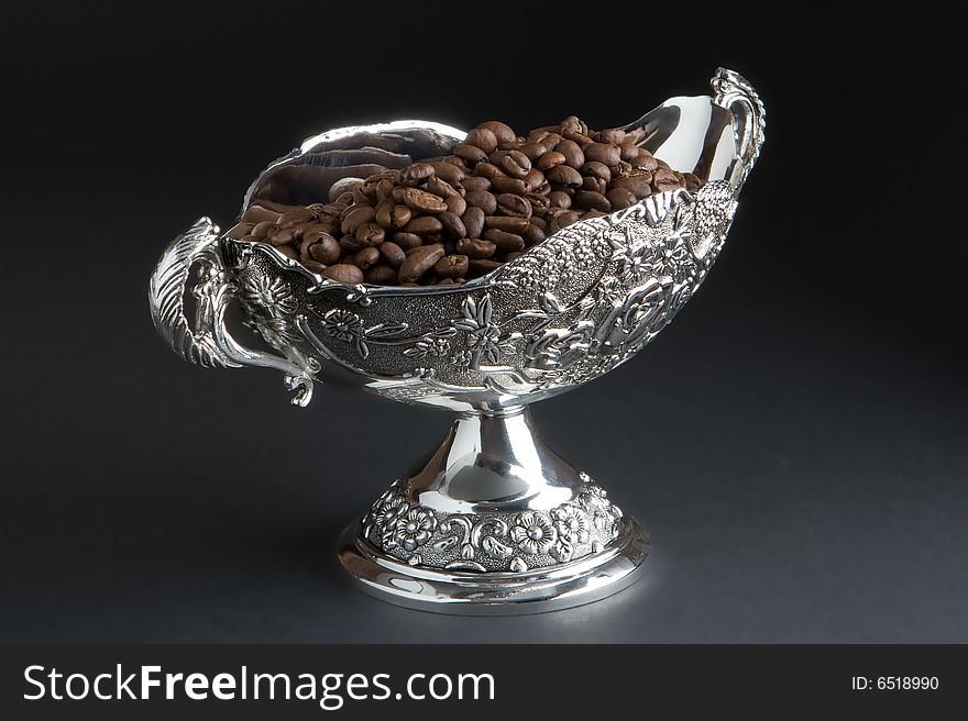 Coffee beans in a silver vase on a dark background. Coffee beans in a silver vase on a dark background