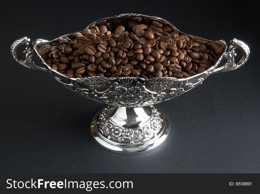 Coffee beans in a silver vase on a dark background