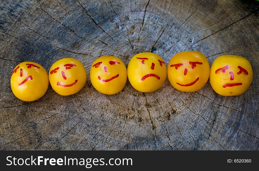 Line of yellow plums painted as emoticons on wood surface. Line of yellow plums painted as emoticons on wood surface