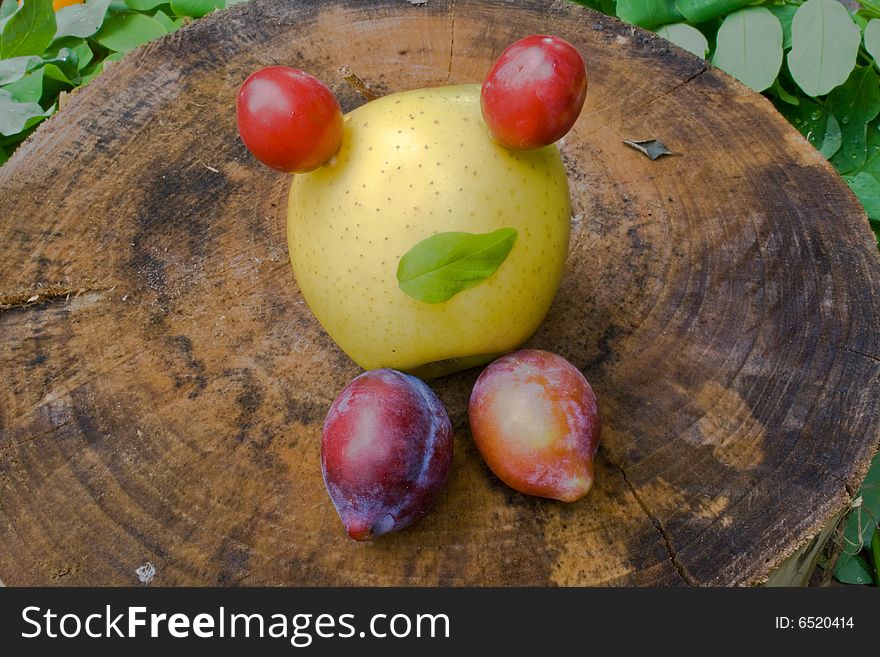 Mister apple with eyes and legs from plums on wood surface