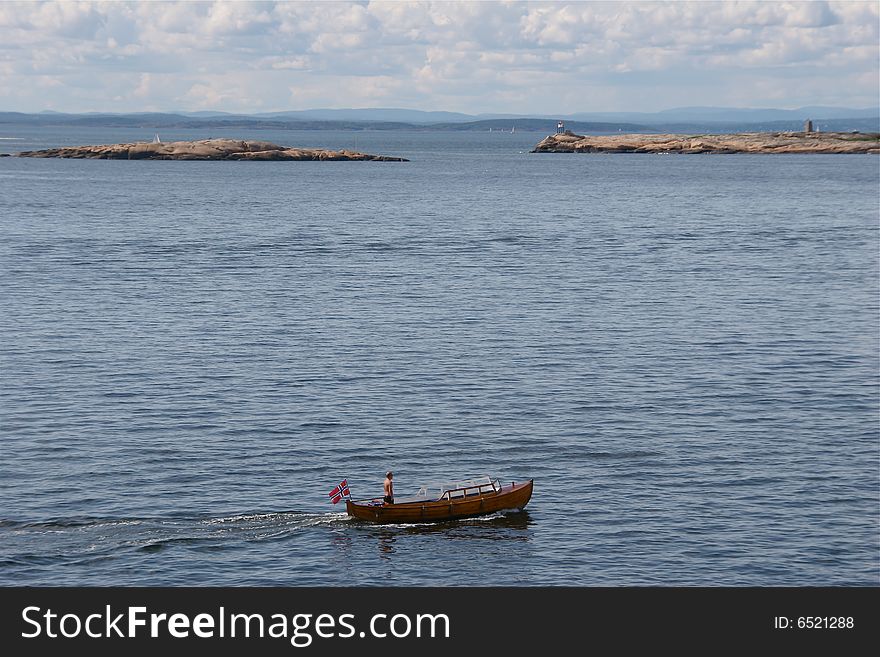 A man standing in his small wooden boat on his way in the fjord. A man standing in his small wooden boat on his way in the fjord