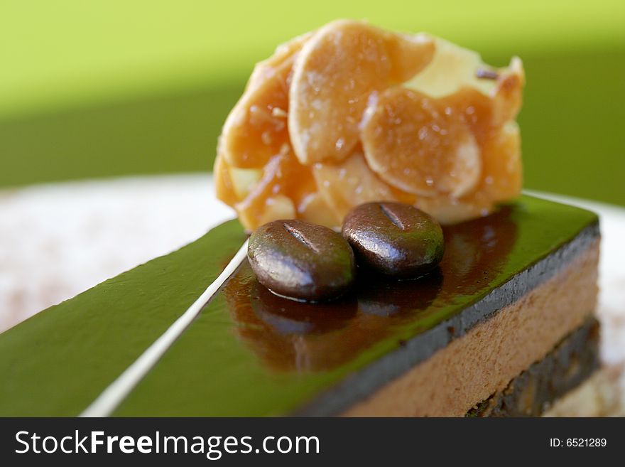 Coffee & chocolate slice, with coffee beans and almond flakes on top, against fresh, contemporary green background. Coffee & chocolate slice, with coffee beans and almond flakes on top, against fresh, contemporary green background