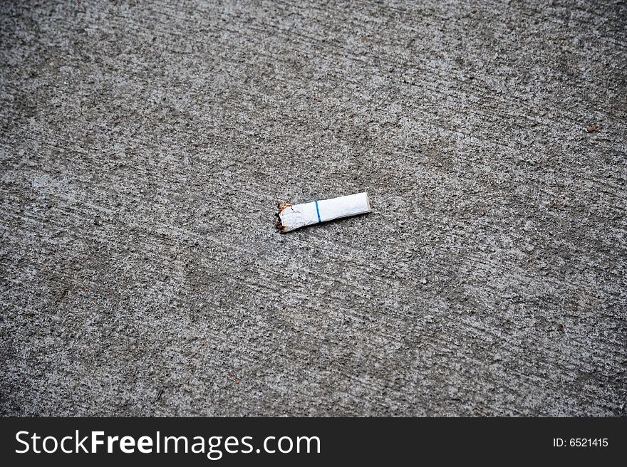 Someone littered the sidewalk with a cigarette butt.