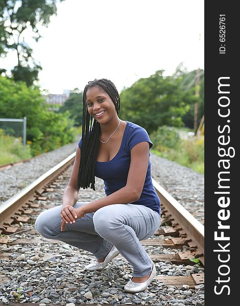 Prety black teenage girl crouching on train tracks. Prety black teenage girl crouching on train tracks