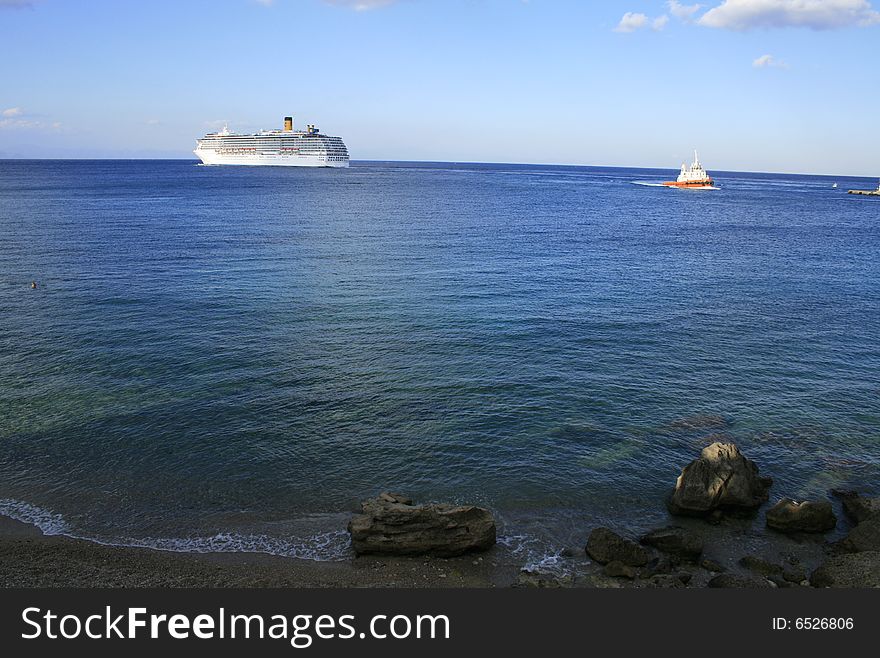 Cruise ship on the blue sea and the sky above with shore and rocks on the front . Cruise ship on the blue sea and the sky above with shore and rocks on the front