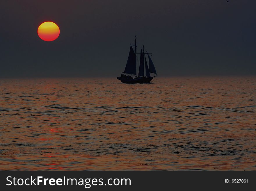 A old style sailing vessel sailing past a setting sun on Lake Michigan. A old style sailing vessel sailing past a setting sun on Lake Michigan