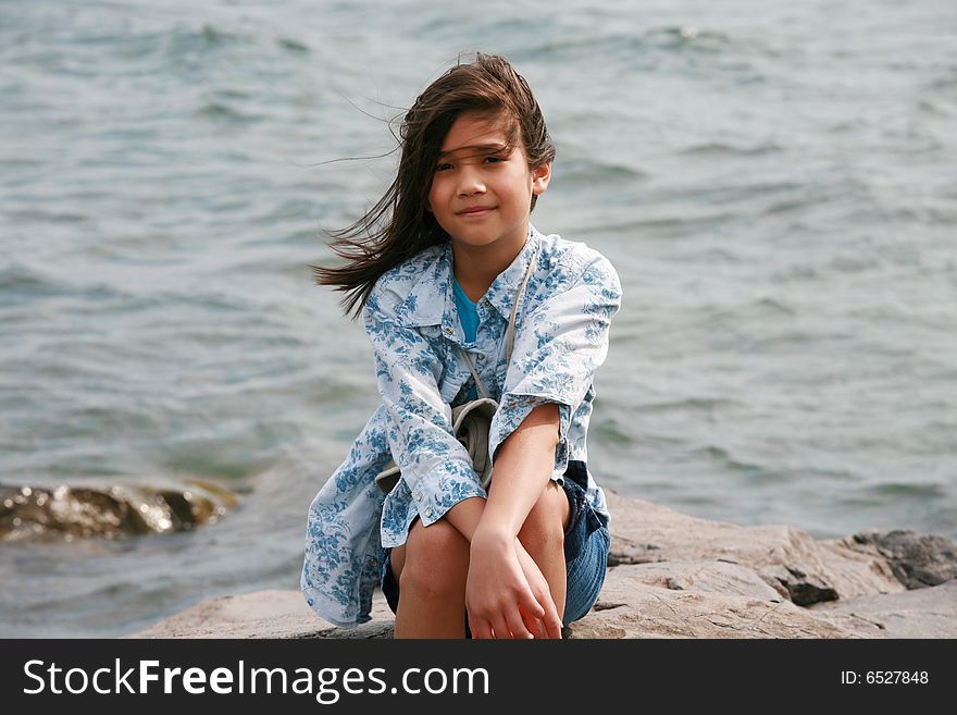 Nine year old girl sitting by lake in summer. Part asian- Scandinavian background.