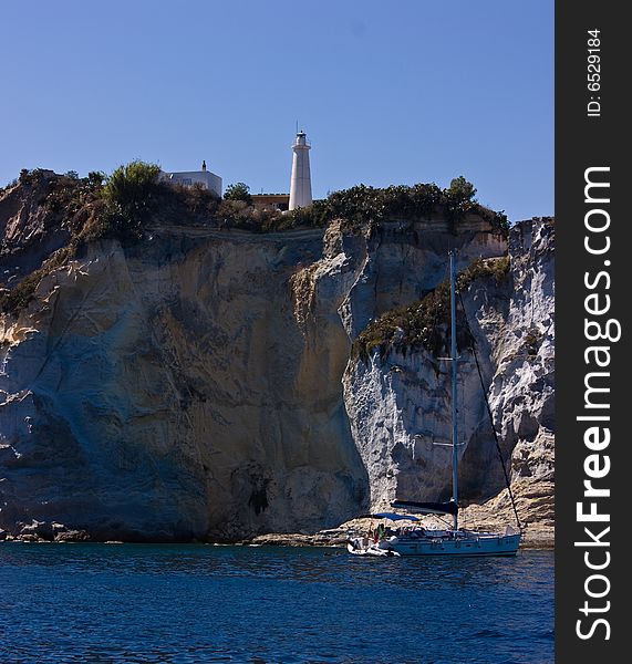 Lighthouse on steep mountain and sail yacht near Ponza island (Italy).