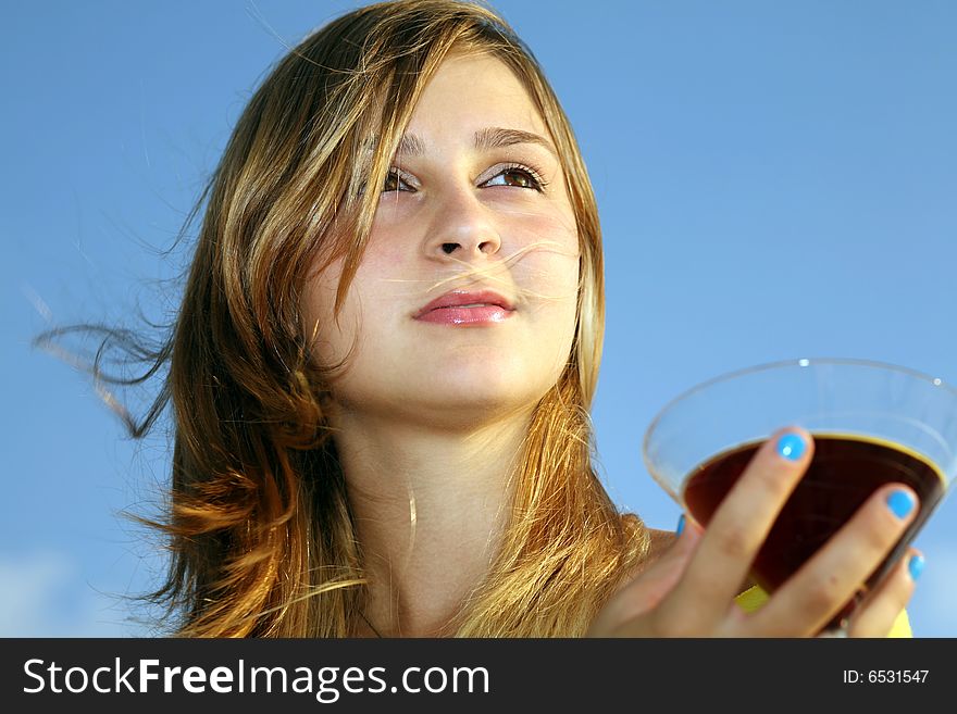 A young beautiful girl with glass of red drink looks far on a background blue sky