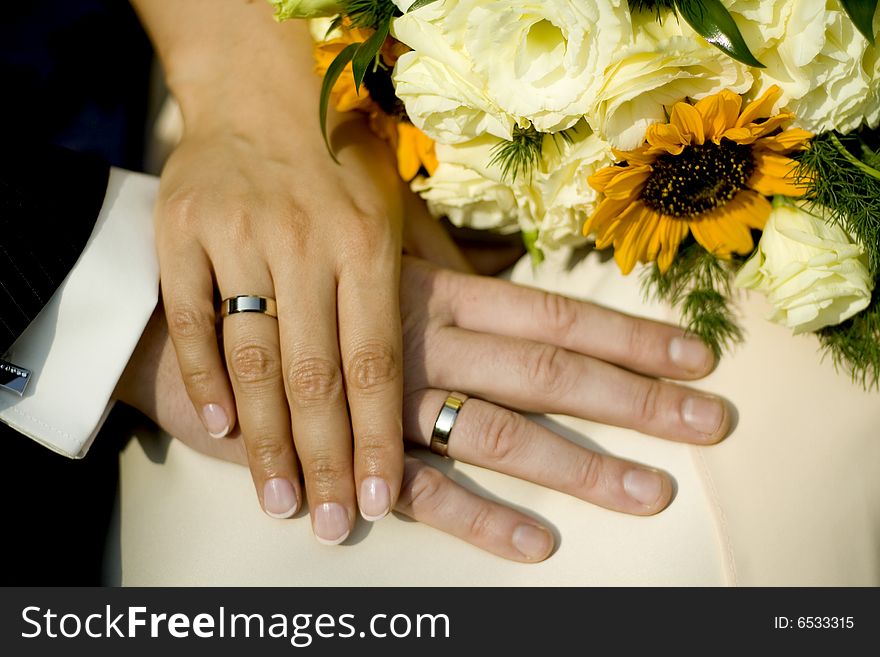 Holding hands of bride and groom with wedding bouquet in the background. Holding hands of bride and groom with wedding bouquet in the background