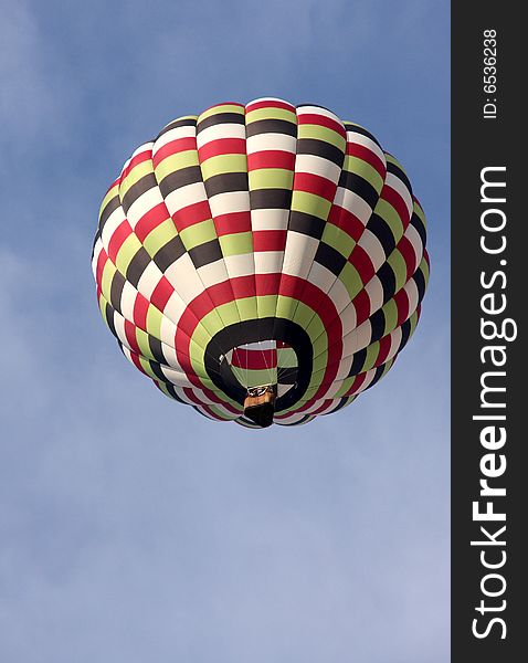 A multi-colored hot air balloon ascending into the clear blue sky