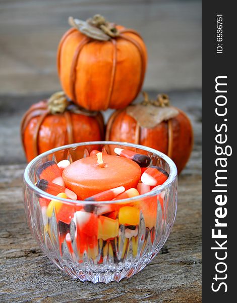 A candle holder full of candy corn and an orange candle with fake pumpkins in the background. A candle holder full of candy corn and an orange candle with fake pumpkins in the background.