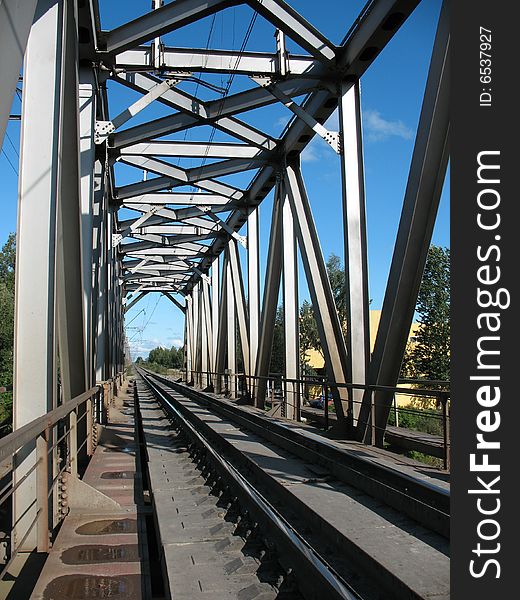 A running away railroad. A permanent way, a macadam, a sleepers and rails. A skylineand a overcast sky.railway bridge