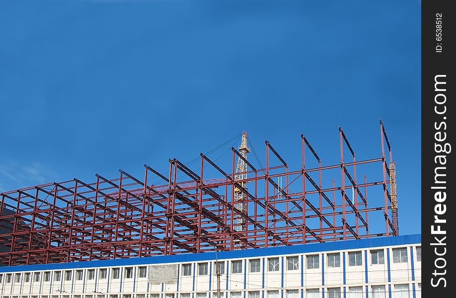 A building site, a hoisting crane and unfinished walls on the blue sky background.