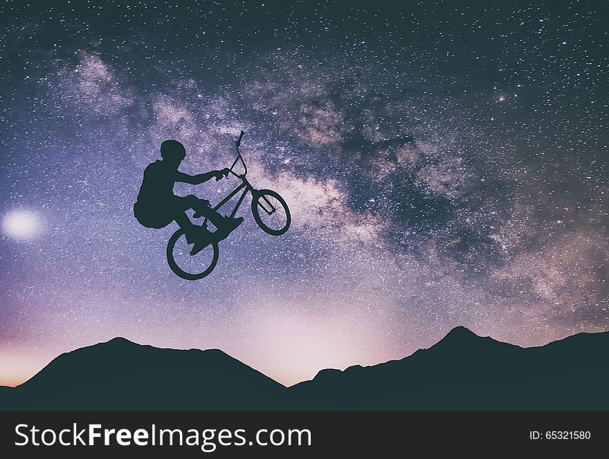 Man riding a bike performing a trick against on Mountain with Milky way. Man riding a bike performing a trick against on Mountain with Milky way.