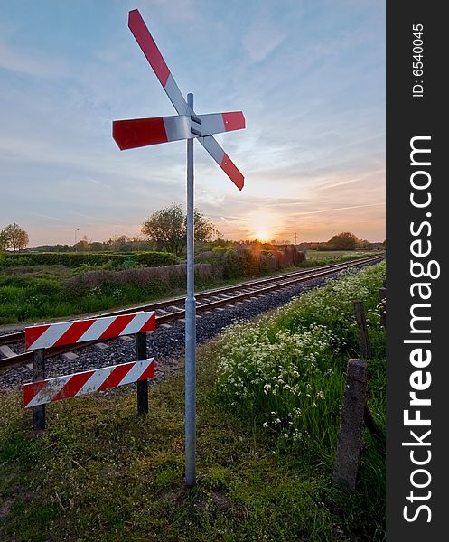 Railway tracks with pastel sunset and traffic sign in a rural scene