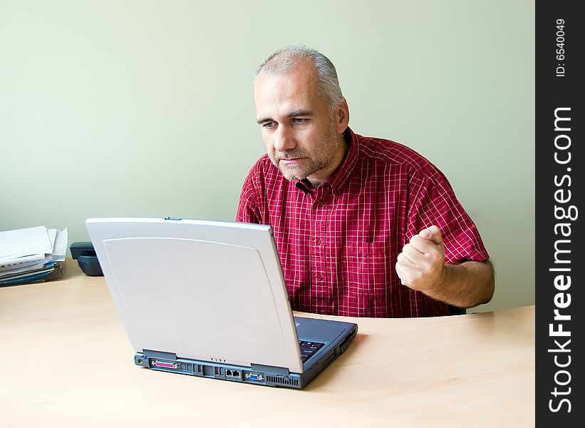 Angry office worker working at the desk with laptop and punching fist on the desk