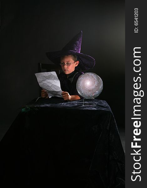 Wizard child reading his spell next to a crystal ball. Wizard child reading his spell next to a crystal ball