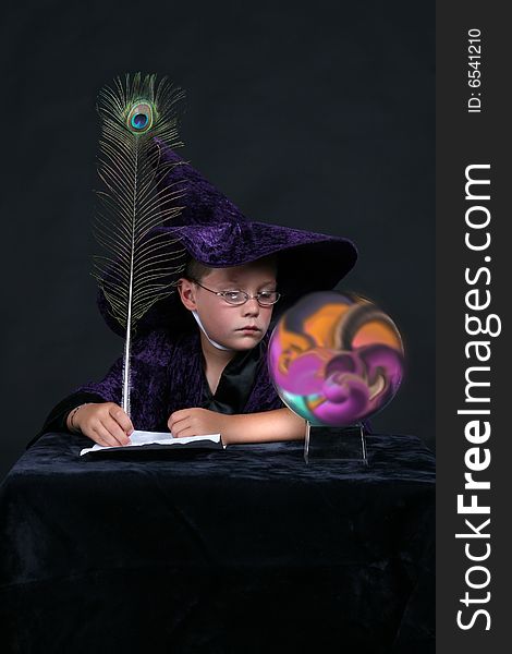 Wizard child with peacock feather pen looking into colorful crystal ball. Wizard child with peacock feather pen looking into colorful crystal ball
